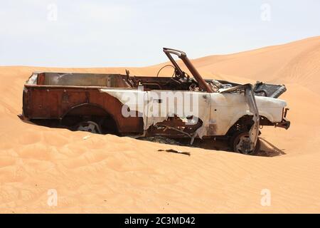 Un relitto del veicolo 4x4 (trazione integrale) bruciato e arrugginito parzialmente sepolto nelle dune di sabbia del deserto arabo. La sabbia lentamente sta travolgendo il relitto. Foto Stock