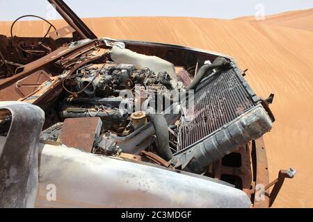 Un relitto del veicolo 4x4 (trazione integrale) bruciato e arrugginito parzialmente sepolto nelle dune di sabbia del deserto arabo. La sabbia lentamente sta travolgendo il relitto. Foto Stock