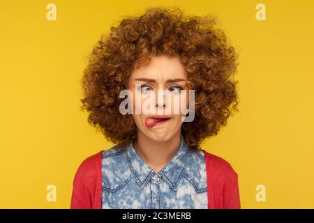 Ritratto closeup di pazza donna con capelli morbidi ricci che dimostrano la lingua fuori e facendo il viso sciocco con occhi incrociati, muto espressione senza cervello. In Foto Stock