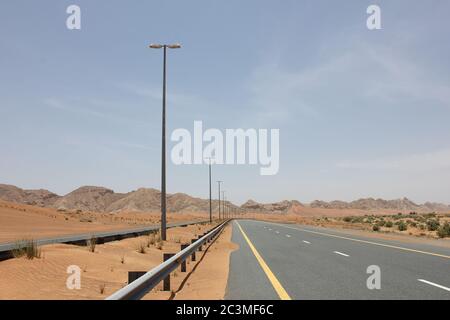 Una moderna autostrada asfaltata a due carrelli taglia le aride dune di sabbia del deserto. Foto Stock