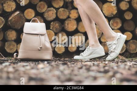 Gambe di una donna in sneakers beige e beige zaino di fronte alla legna impilata Foto Stock
