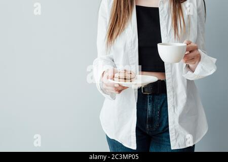 Ragazza in T-shirt bianca e Jeans tiene tazza di caffè e piatto di Macaron francesi Foto Stock