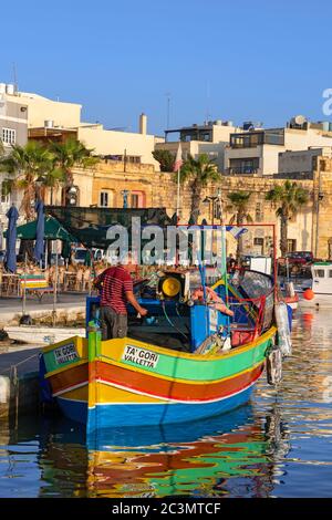 Pescatore su una tradizionale barca Luzzu nel porto di Marsaxlokk villaggio di pescatori sull'isola di Malta nel Mar Mediterraneo Foto Stock