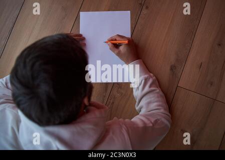 un uomo scrive su un foglio bianco di carta su uno sfondo grigio Foto Stock