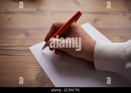 un uomo scrive su un foglio bianco di carta su uno sfondo grigio Foto Stock