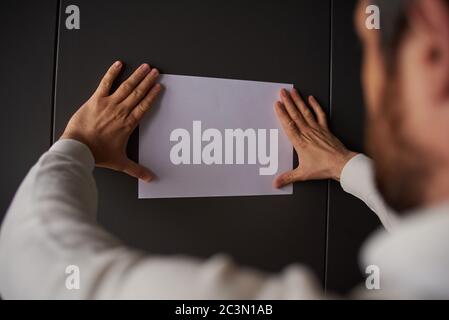 un uomo scrive su un foglio bianco di carta su uno sfondo grigio Foto Stock