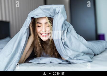 Donna sorridente sotto un piumone nella sua camera da letto Foto Stock