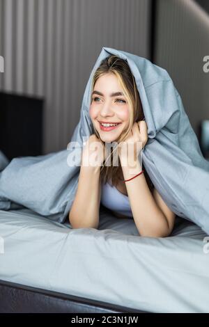 Donna sorridente sotto un piumone nella sua camera da letto Foto Stock