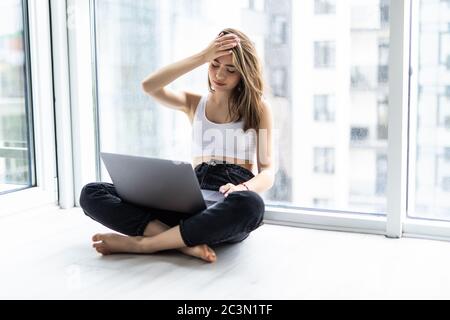 Donna scioccata seduta sul davanzale con una tazza di caffè mentre si usa il computer portatile Foto Stock