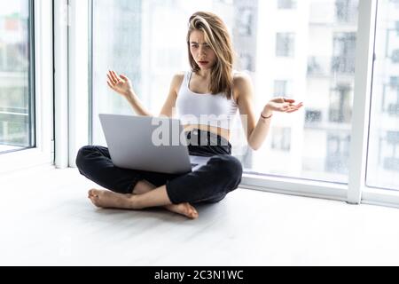 Donna scioccata seduta sul davanzale con una tazza di caffè mentre si usa il computer portatile Foto Stock