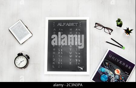 Alfabeto scritto su una piccola lavagna sul tavolo vicino libri e bicchieri sotto le luci Foto Stock