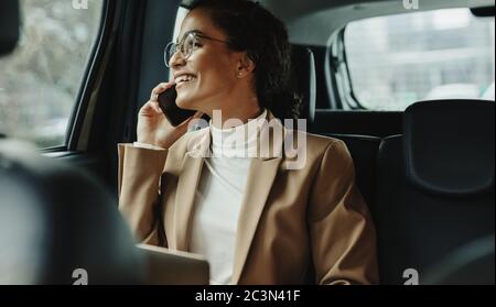 Donna d'affari seduto sul sedile posteriore della sua auto e che parla sul telefono cellulare. Donna d'affari che usa il telefono mentre viaggia in auto. Foto Stock