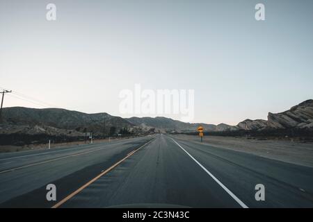 Empty Highway in California subito dopo il tramonto con il cartello giallo e le montagne in lontananza durante il Coronavirus Pandemic Foto Stock
