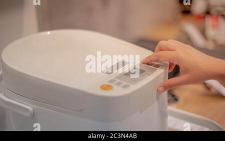 Mano femminile premendo il pulsante del nuovo cuoci riso moderno in cucina per preparare il cuoco per la famiglia, nuova macchina elettronica tecnologia co Foto Stock