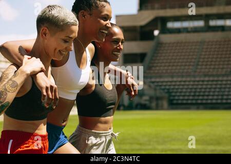 Gruppo di tre atleti femminili che camminano insieme sul campo sportivo dopo la sessione di allenamento. Sportivo multietnico dopo un allenamento a stadi Foto Stock