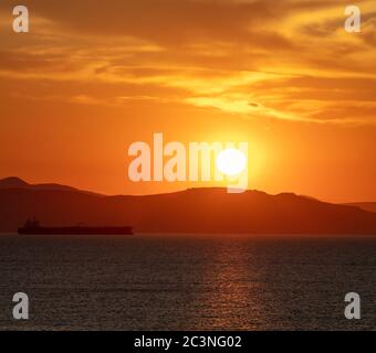 Tramonto arancione nuvoloso paesaggio sull'acqua di mare. Spettacolare e magico tramonto mare in Grecia mar Egeo. Crepuscolo, sfondo dell'alba. Terra e orang dell'isola oscura Foto Stock