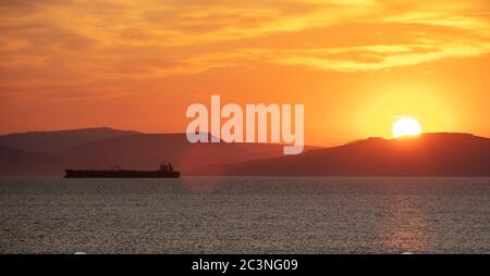 Tramonto arancione nuvoloso paesaggio sull'acqua di mare. Spettacolare e magico tramonto mare in Grecia mar Egeo. Crepuscolo, sfondo dell'alba. Terra e orang dell'isola oscura Foto Stock