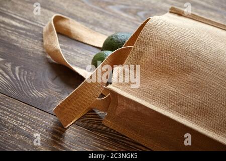 Borsa riutilizzabile con frutta fresca. Materiale naturale eco-compatibile. Avocado verde, sacco di hessian o iuta su tavolo di legno marrone. Utile pro organico Foto Stock