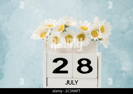 Calendario cubo bianco per luglio decorato con fiori margherita su blu con spazio copia Foto Stock