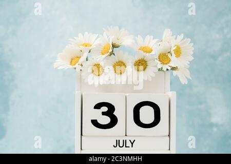 Calendario cubo bianco per luglio decorato con fiori margherita su blu con spazio copia Foto Stock