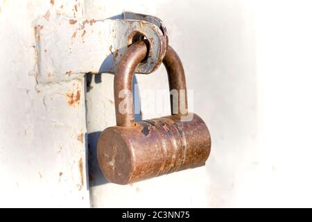 Primo piano di illuminato da sole vecchio lucchetto di metallo grezzo su garage o fienile cancello di ferro. Tecnologia obsoleta, sicurezza, sicurezza e protezione dal concetto di ladri. Foto Stock