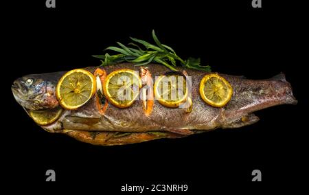 Trota deliziosa al forno farcita con erbe e spezie, ricoperta di fette di limone su fondo nero Foto Stock