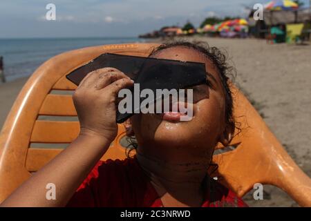 Un bambino usa pezzi di vetro nero per guardare una parziale eclissi solare sulla costa di Lhokseumawe City.The fenomeno di un'eclissi solare è visto in parte nella città di Lhokseumawe, provincia di Aceh. Il fenomeno dell'Eclipse solare anulare (GMC) è in parte diverso quest'anno dall'anno precedente perché coincide con il solstizio estivo, il cosiddetto anello di fuoco solstizio. Secondo l'Istituto di Aviazione e spazio (Lapan), l'anello di fuoco solstizio è piuttosto raro perché è avvenuto per l'ultima volta nel 1648 e sarà ripetuto il 21 giugno 2039. Foto Stock