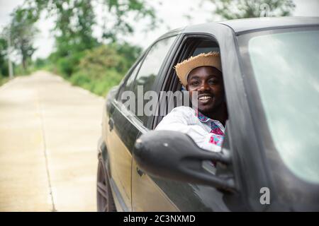 Uomo africano sorridente mentre si siede in un'auto con finestrino anteriore aperto Foto Stock