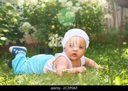 ritratto esterno di un bambino su tutte le farine. strisciando in ginocchio bambino sull'erba in un parco estivo. Foto Stock