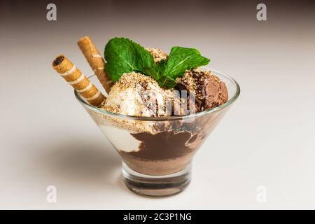 Gelato al cioccolato e alla vaniglia ricoperto di frutta secca macinata e sciroppo di cioccolato, guarnito con cialde di cioccolato e menta, servito in un bicchiere trasparente Foto Stock