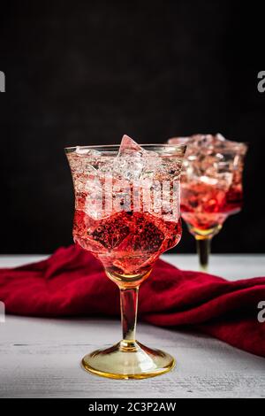 Un primo piano di due splendidi cocktail rinfrescanti con ghiaccio, tavolo di legno bianco, sfondo scuro, tovagliolo rosso Foto Stock