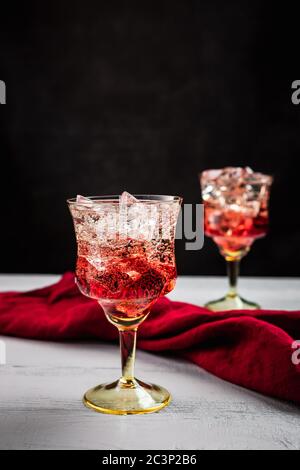 Due splendidi cocktail rinfrescanti con ghiaccio, tavolo di legno bianco, sfondo scuro, tovagliolo rosso Foto Stock