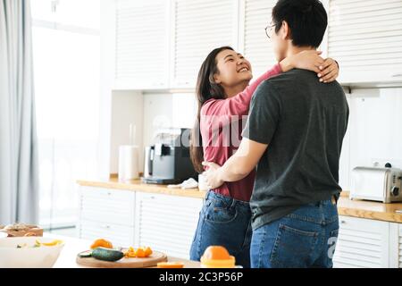 Bella giovane coppia asiatica felice abbracciando mentre si sta in piedi in cucina Foto Stock