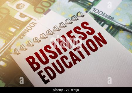 Parole di educazione commerciale a pagina di copybook messo su banconote da 100 euro. Messa a fuoco morbida. Studio del concetto MBA Foto Stock