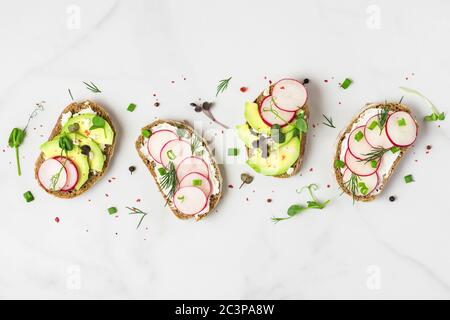 Salutare avocado primaverile e arrosti con formaggio casolare, germogli di piselli e pepe su tavolo di marmo bianco per una sana colazione dietetica. Vista dall'alto Foto Stock