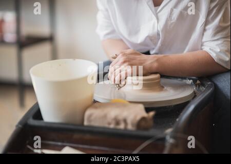 Primo piano di un ceramista irriconoscibile che forma un vaso di argilla lavorato a mano utilizzando un attrezzo speciale e un cerchio di vasaio. Foto Stock