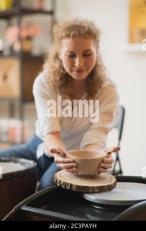 Il vasaio femmina ha finito di fare un vaso di argilla rimuoverlo dalla ruota del vasaio. Creazione vaso di argilla bianca. Produzione di prodotti ceramici da argilla bianca Foto Stock
