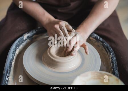 Primo piano di un ceramista irriconoscibile che forma un vaso di argilla lavorato a mano utilizzando un attrezzo speciale e un cerchio di vasaio. Foto Stock