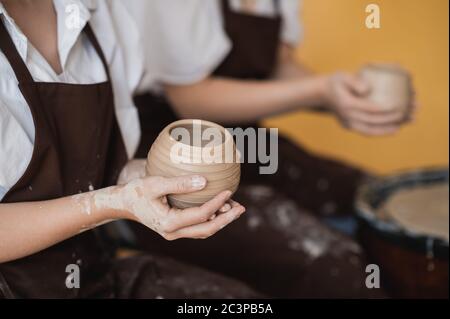 Le vaschette femmina finì di fare un vaso di argilla rimuoverlo dalla ruota del vasaio. Creazione vaso di argilla bianca. Produzione di prodotti ceramici da argilla bianca Foto Stock