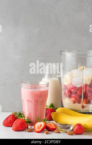 Bicchiere di frullato di fragola e banana vegan o frullato di latte di mandorla con ingredienti freschi e succosi nel frullatore per una bevanda sana. verdi Foto Stock