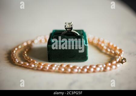 Primo piano di un anello di diamante in una scatola verde sul tavolo con una collana di perle sotto le luci Foto Stock