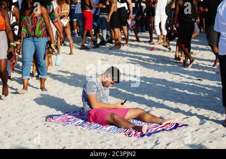 MIAMI - 16 MARZO 2019: Un giovane si siede con il telefono ad un incontro di studenti universitari che celebrano la pausa primaverile a South Beach. Foto Stock