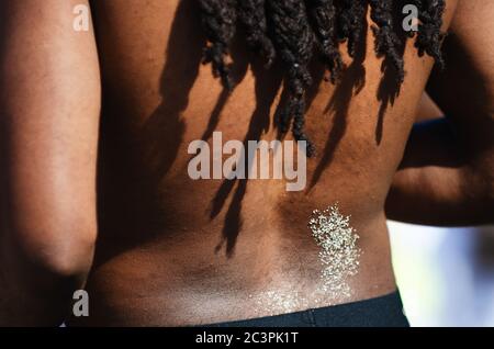 Primo piano di una schiena sabbiosa con dreadlock che getta ombre sulla pelle marrone sul retro di un uomo americano alla spiaggia di Miami, Florida, USA Foto Stock