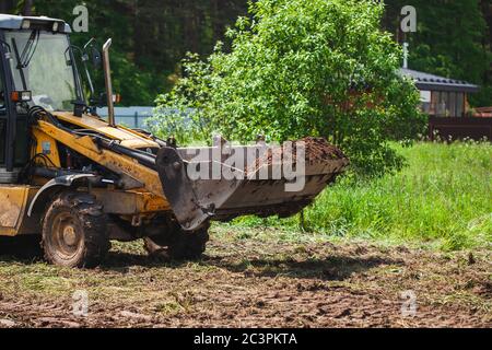 Compensazione e livellamento di un terreno privato. Terra azionata da un escavatore giallo in una benna larga Foto Stock
