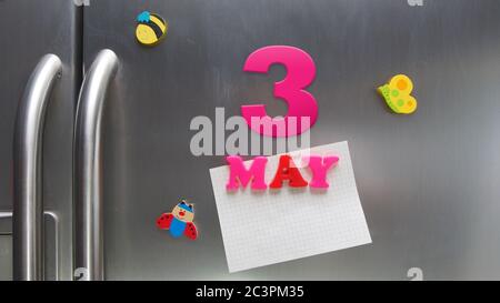 Data di calendario del 3 maggio fatta con lettere magnetiche di plastica che tengono una nota di carta grafica sul frigorifero della porta Foto Stock