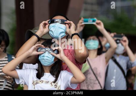 Hong Kong, Cina. 21 Giugno 2020. La gente guarda un'eclissi solare parziale anulare attraverso uno speciale visore dell'eclissi lungo una passeggiata a Hong Kong. Un'eclissi solare parziale si verifica quando una parte della Terra è ingolfata dall'ombra (penombra) gettata dalla Luna mentre passa tra il nostro pianeta e il Sole in un allineamento imperfetto. Credit: May James/ZUMA Wire/Alamy Live News Foto Stock