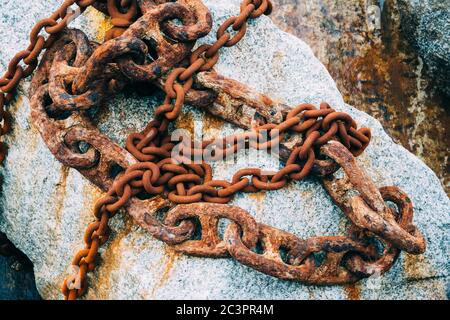 Scatto orizzontale di molte catene arrugginite di diverse dimensioni su una grande pietra Foto Stock