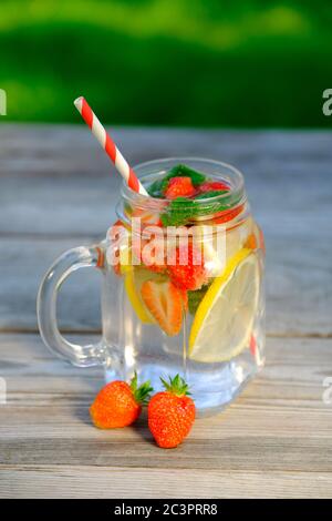 Bicchiere di bevanda estiva con fragole, fette di limone e menta. Cocktail rinfrescante, punch detox fatto in casa, limonata fredda. Foto Stock