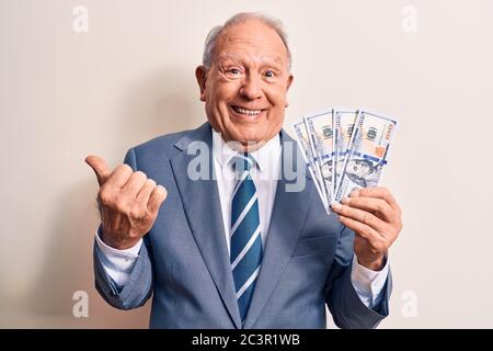 Uomo d'affari con capelli grigi senior che indossa la tuta tenendo un mazzo di banconote in dollari urlando orgoglioso, celebrando la vittoria e il successo molto eccitato Foto Stock