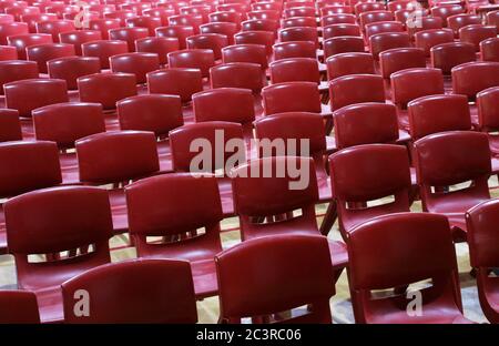 Masse di rosso stampato massa ha prodotto sedie in plastica stile scuola allineati ordinatamente in file vuote pronti per l'assemblaggio o una convenzione Foto Stock